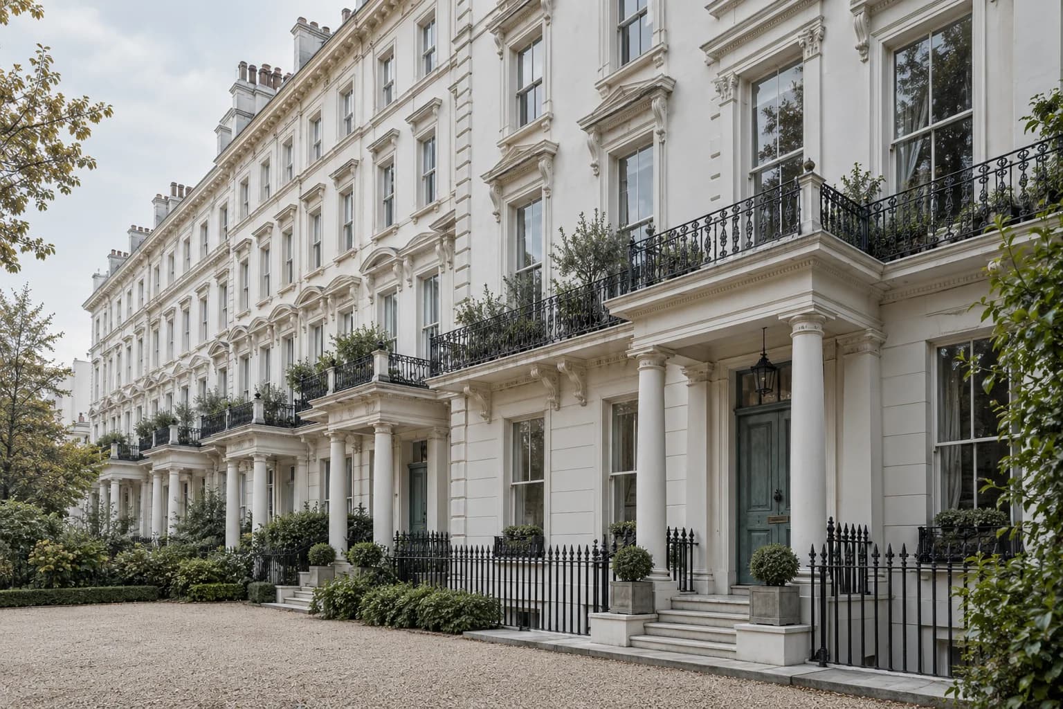 Tall pale stucco terraces with timber sash windows and iron railings beside a leafy garden